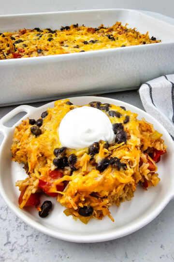 chicken taco casserole on a white plate with a dollop of sour cream on top.