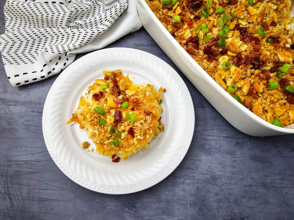 Million Dollar Potato Casserole served on a white plate beside the baked casserole dish.