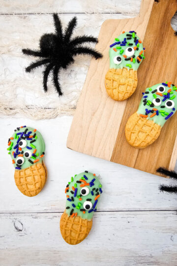 Monster Nutter Butter Halloween cookies arranged with black spider decorations and a wooden serving board.