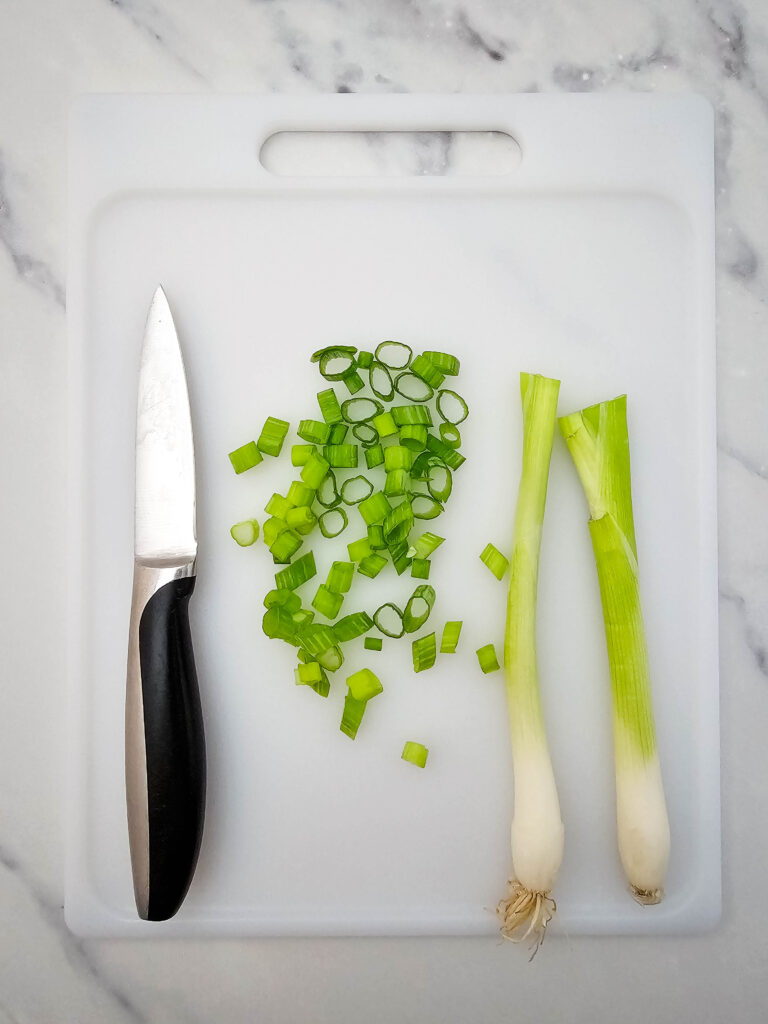 Sliced green onions on a white cutting board with a knife.