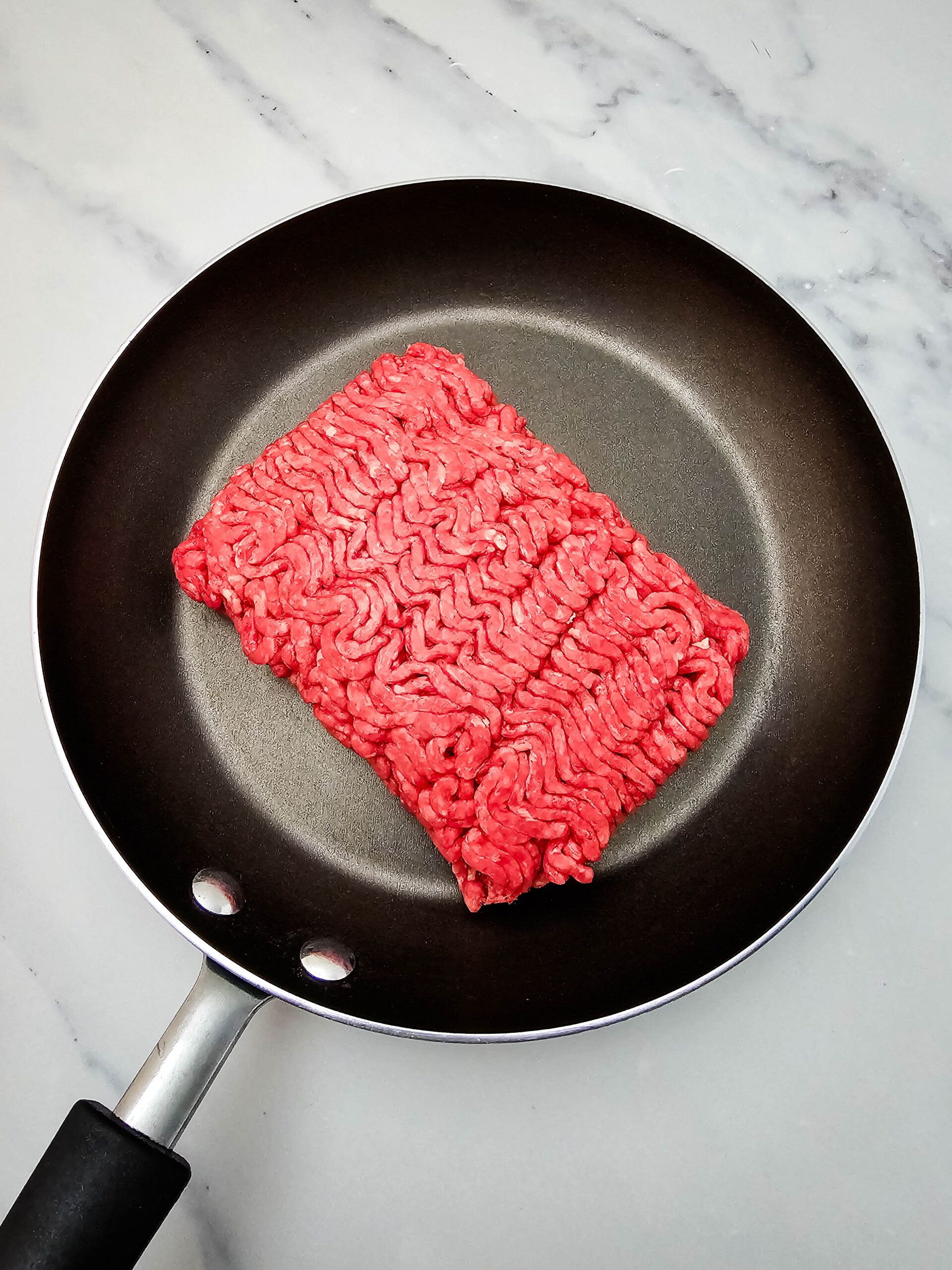 Raw ground beef in a skillet before cooking for Hobo Casserole.