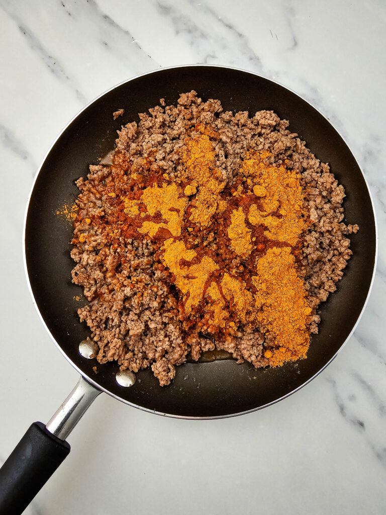 Taco seasoning and water added to cooked ground beef in a skillet.