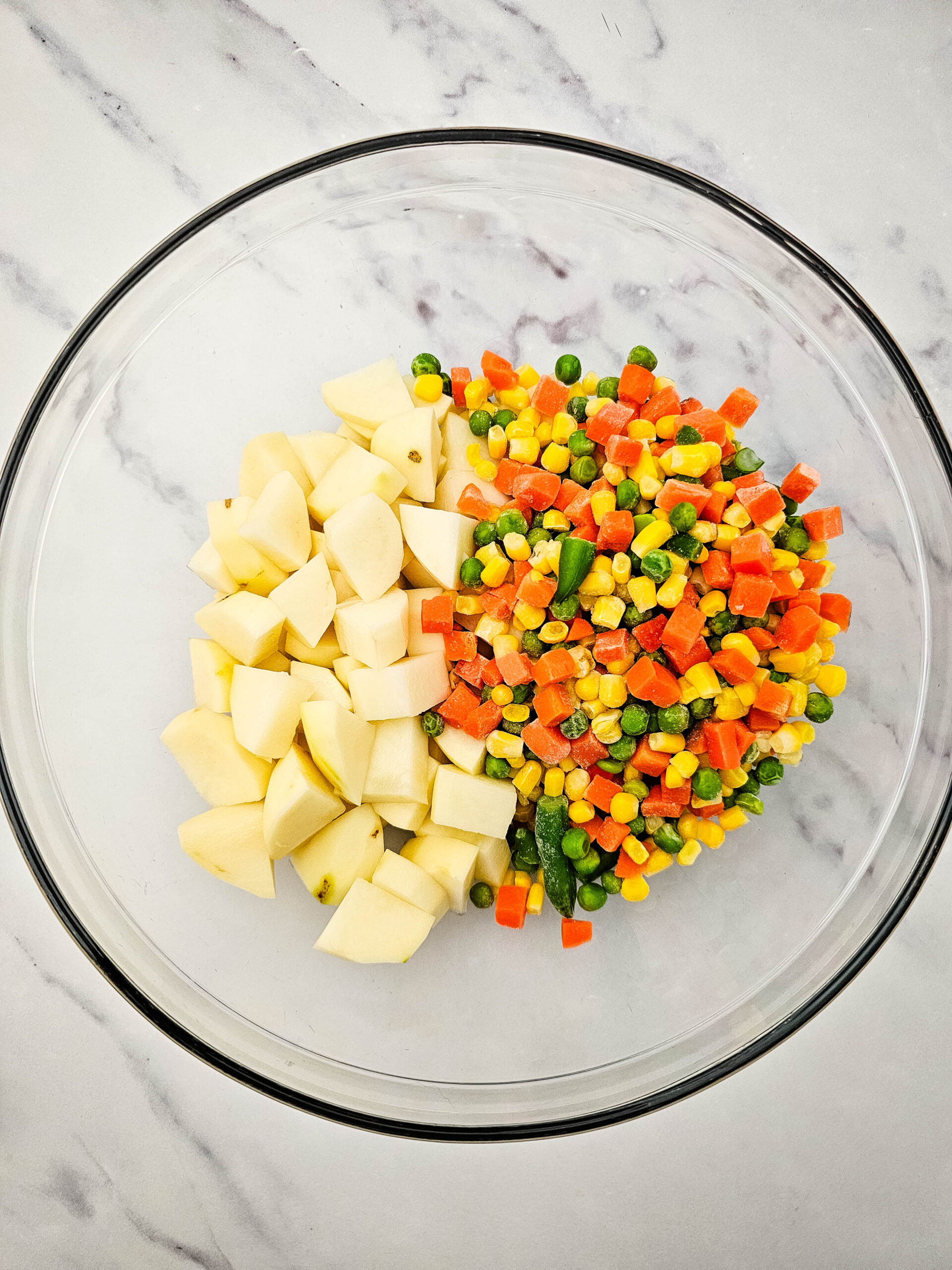 Diced potatoes and mixed vegetables in a glass bowl for Hobo Casserole.