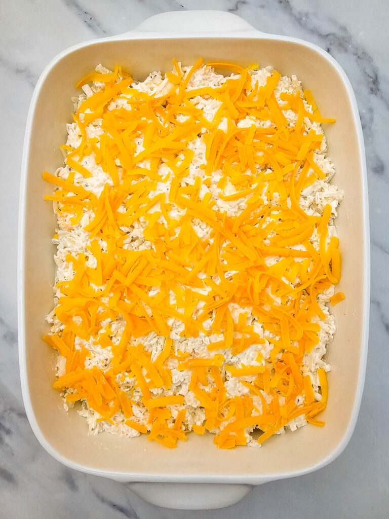 Hashbrown casserole mixture topped with shredded cheddar cheese before baking.