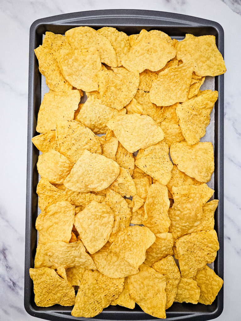 Tortilla chips arranged in an even layer on a baking sheet for sheet pan ground beef nachos.