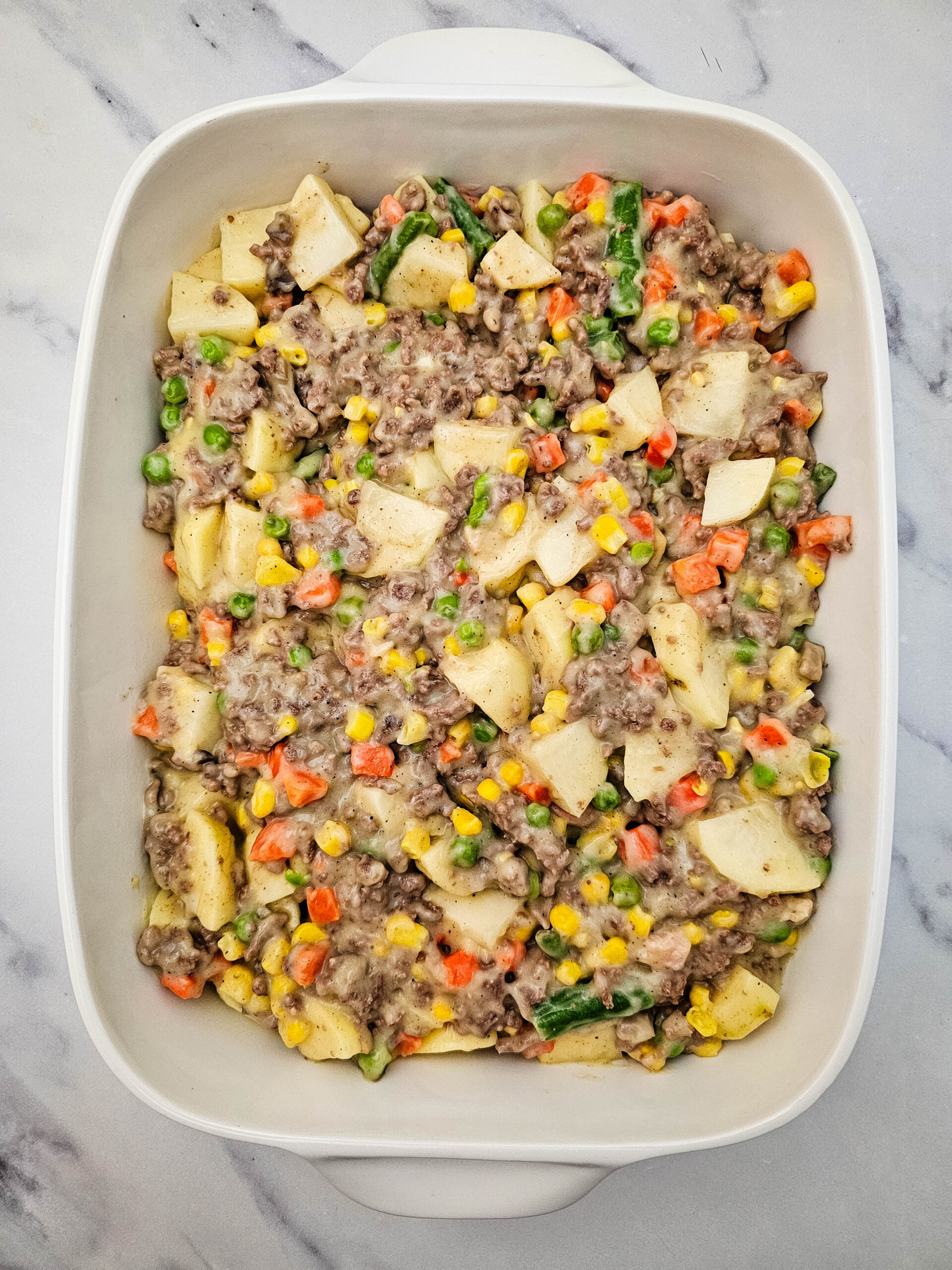 Hobo Casserole mixture with ground beef, potatoes, vegetables, and creamy sauce spread in a baking dish.