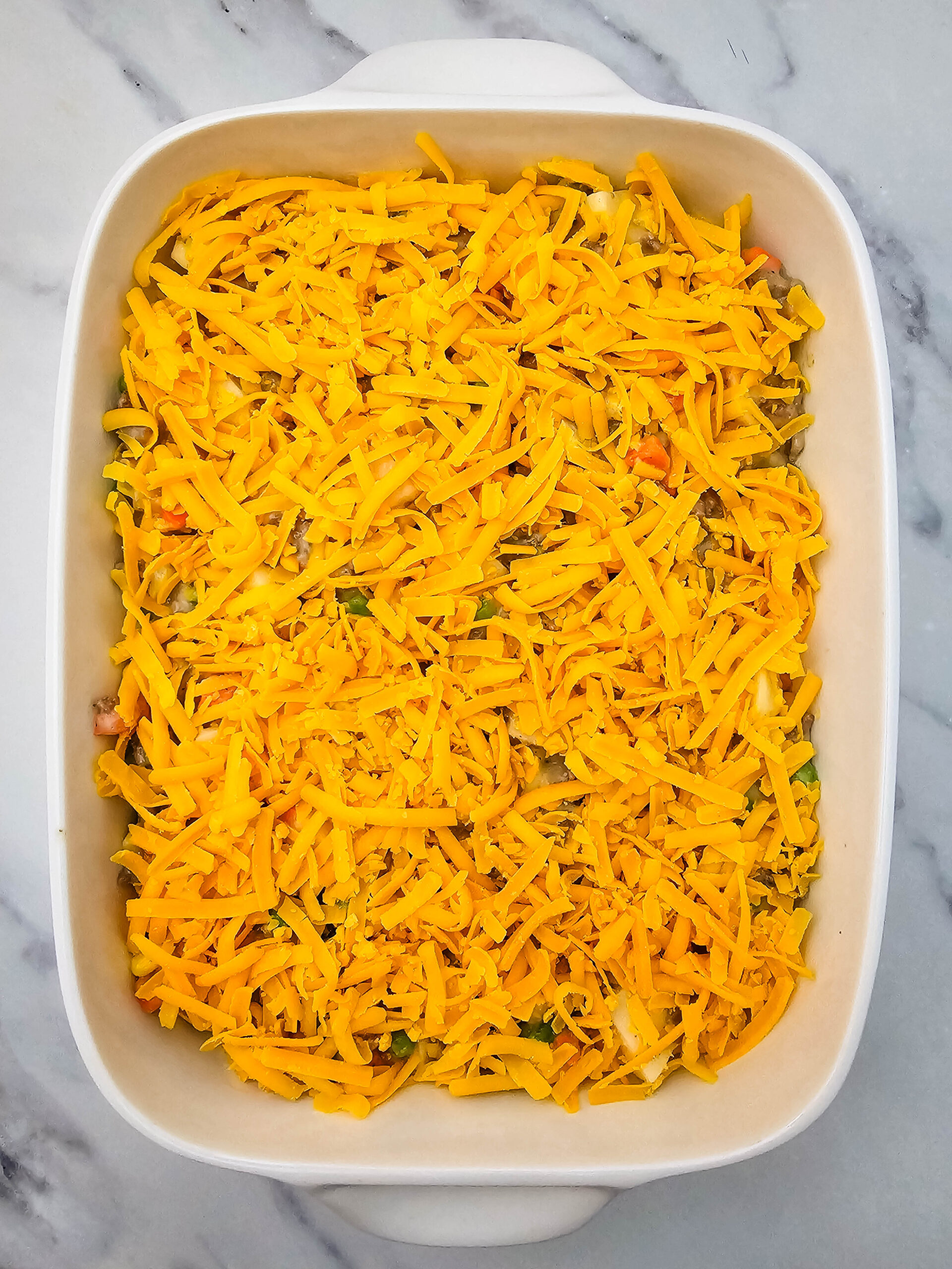 Hobo Casserole topped with shredded cheddar cheese before baking.